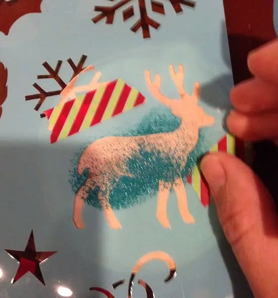 Stenciling a deer onto a wood slice coaster with teal paint