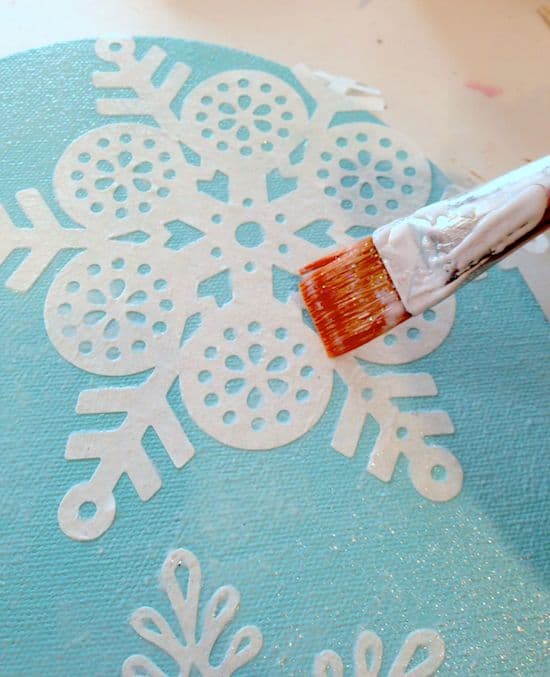 Mod Podging paper snowflakes to the front of a painted oval canvas