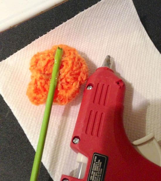 Hot gluing a crochet flower to a dowel rod with a hot glue gun