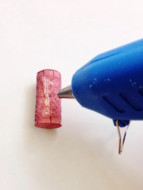 Placing a bead of hot glue on a wine cork using a hot glue gun
