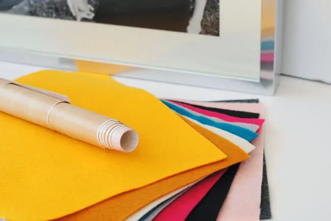 Stack of colorful felt with a woodgrain roll of contact paper on top