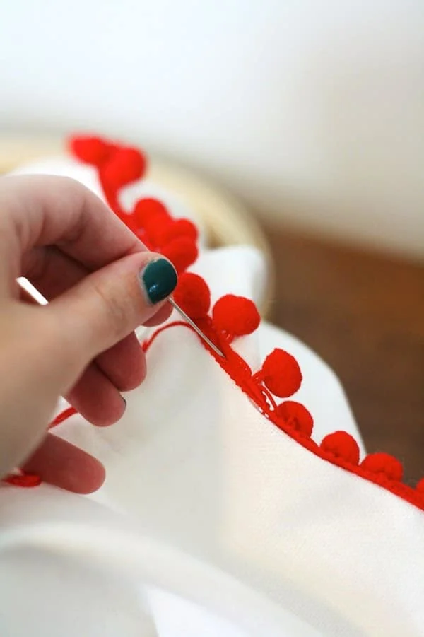 Stitching a red pom pom border on a pillowcase by hand
