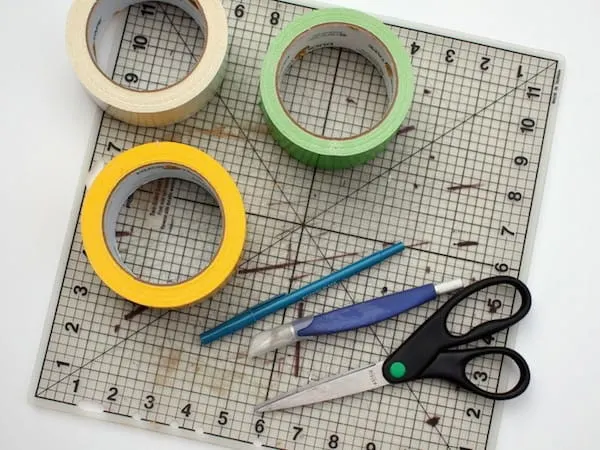 Rolls of duct tape sitting on a craft mat with scissors, a pen, and a craft knife