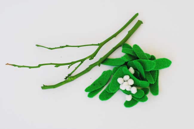 Green painted twigs, green felt pieces, and small white pom poms