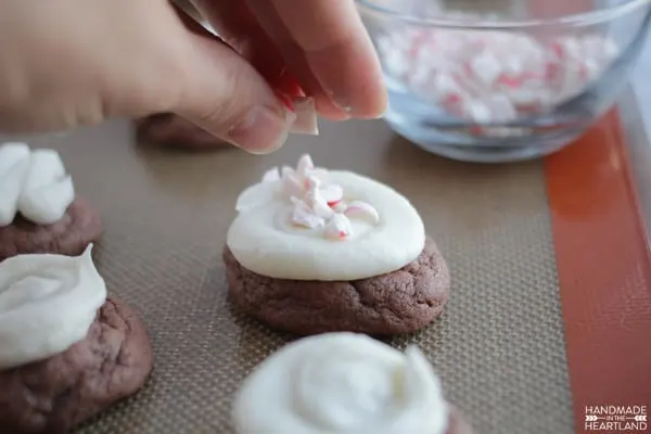 Sprinkling peppermint pieces on top of iced chocolate pudding cookies