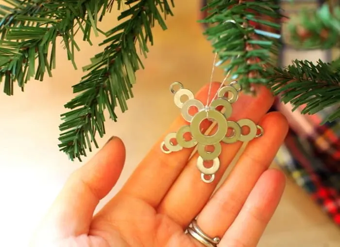 A hand showing a DIY star ornament hanging from a Christmas tree