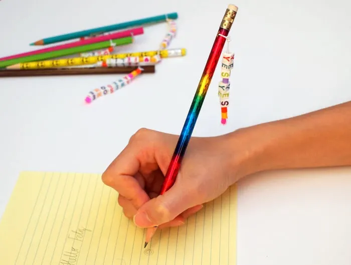 Child writing with a personalized pencil on a yellow piece of paper