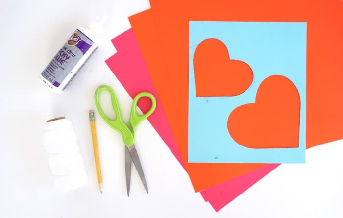 Pink and orange paper, a heart template, Tacky glue, scissors, a pencil, and twine