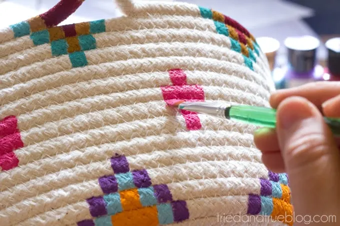 Adding pink paint onto a basket with a paintbrush