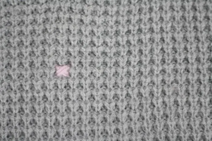 Small pink cross stitch on the front a gray sweater