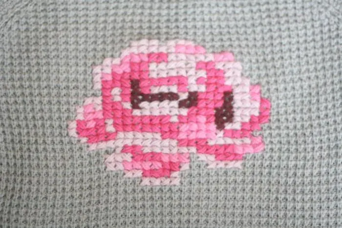 Rose cross stitched onto the front of a gray sweater