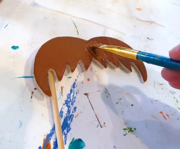 Painting a wooden mustache piece with brown paint