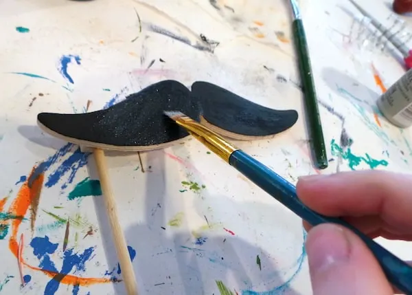 Painting a mustache with black extreme glitter