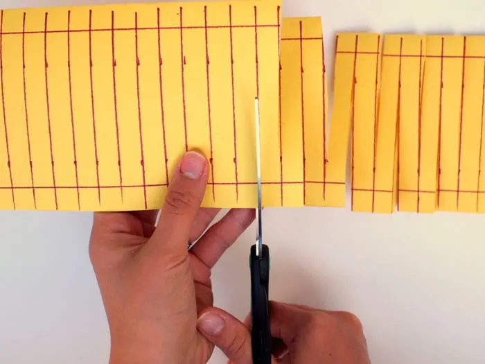 Cutting the yellow construction paper on the lines with a pair of scissors