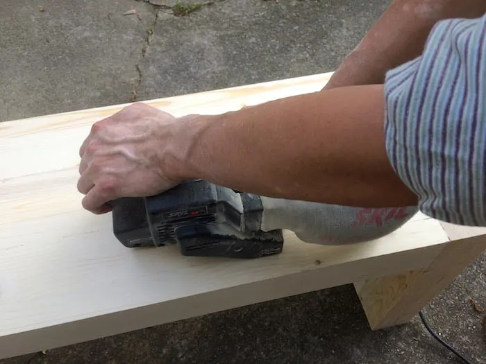 Sanding the top of a bench with a belt sander
