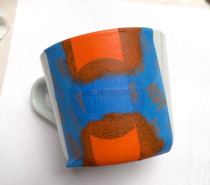 Painter's tape applied to a mug with orange paint on top