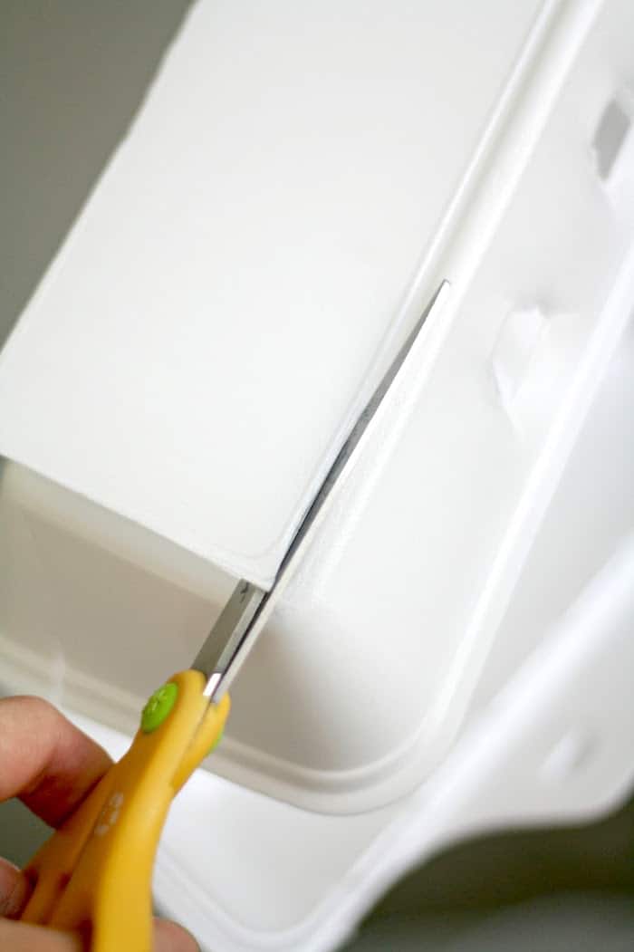 Cutting out a portion of the takeout box with yellow handled scissors