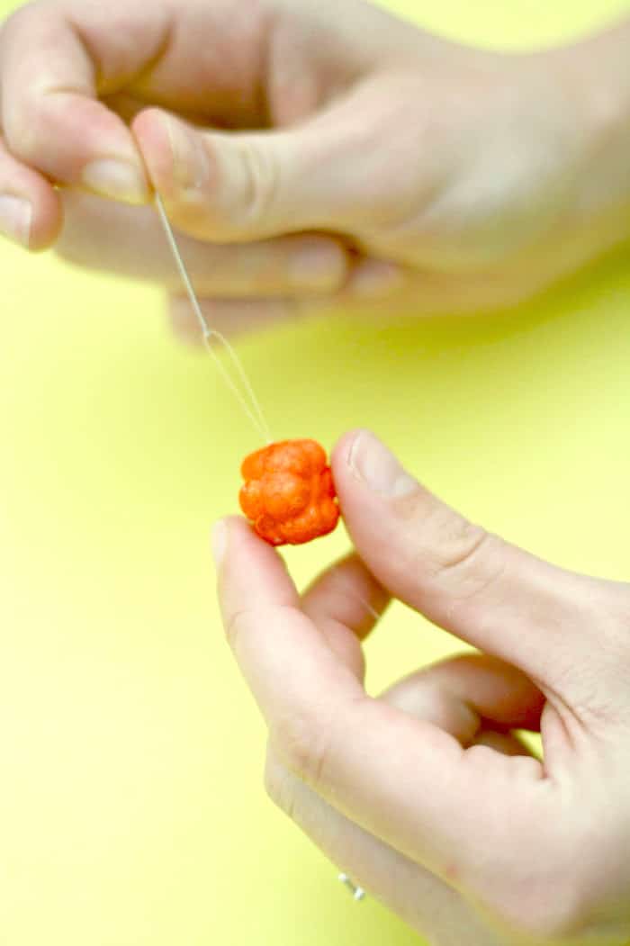 Threading a needle and fishing line through a small foam pumpkin
