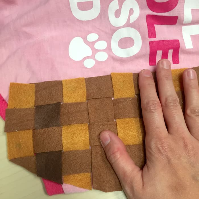 Hand pressing the woven brown felt down onto the hot glue on the dog shirt