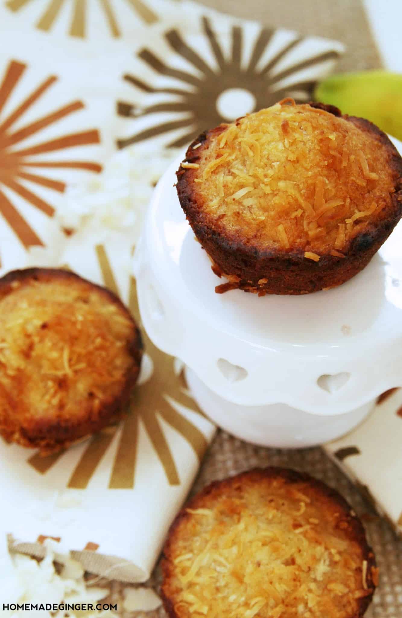 Toasted coconut banana muffins on a table with one on a small white glass pedestal
