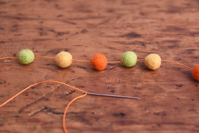 Stringing felt balls on orange thread with a needle attached