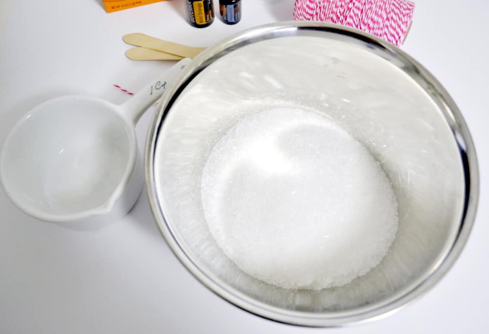 Epsom salt and baking soda in a metal mixing bowl with a white measuring cup sitting next to the bowl