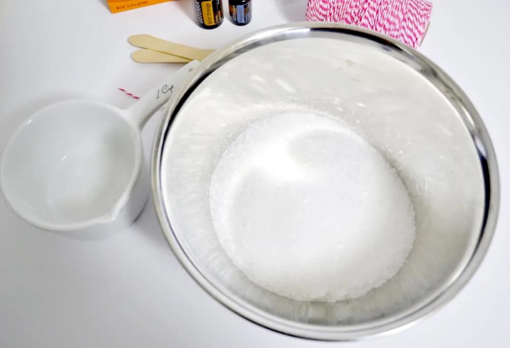 Epsom salt and baking soda in a metal mixing bowl with a white measuring cup sitting next to the bowl