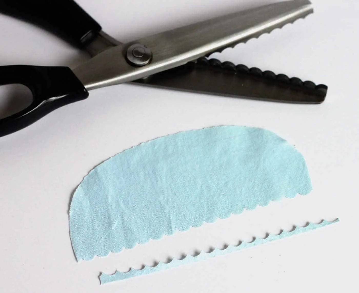 Trimming a piece of blue fabric with scalloped scissors