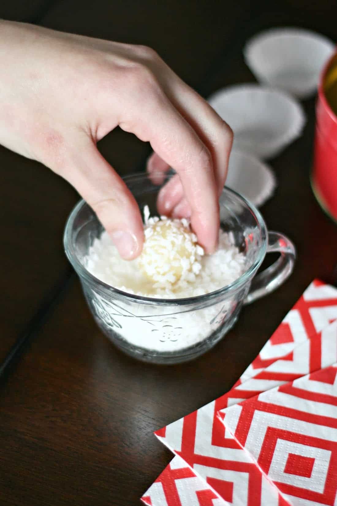 Dipping a beijinho in a glass container with shredded coconut