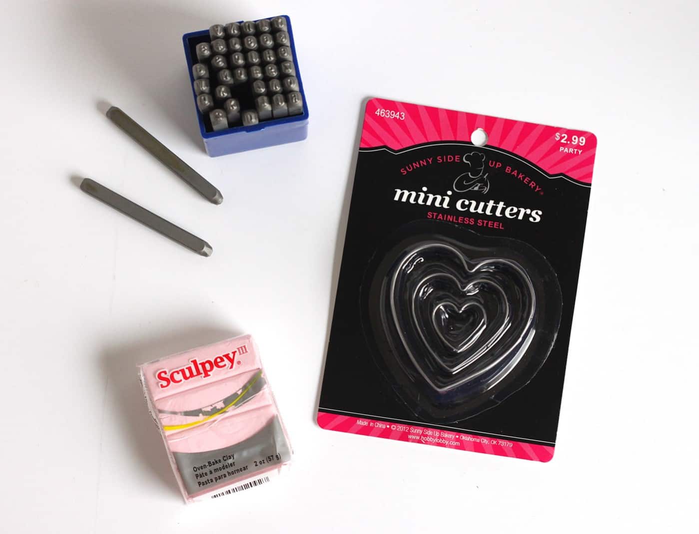 Pink Sculpey clay, mini clay cutters in heart shapes, and letter metal stamps