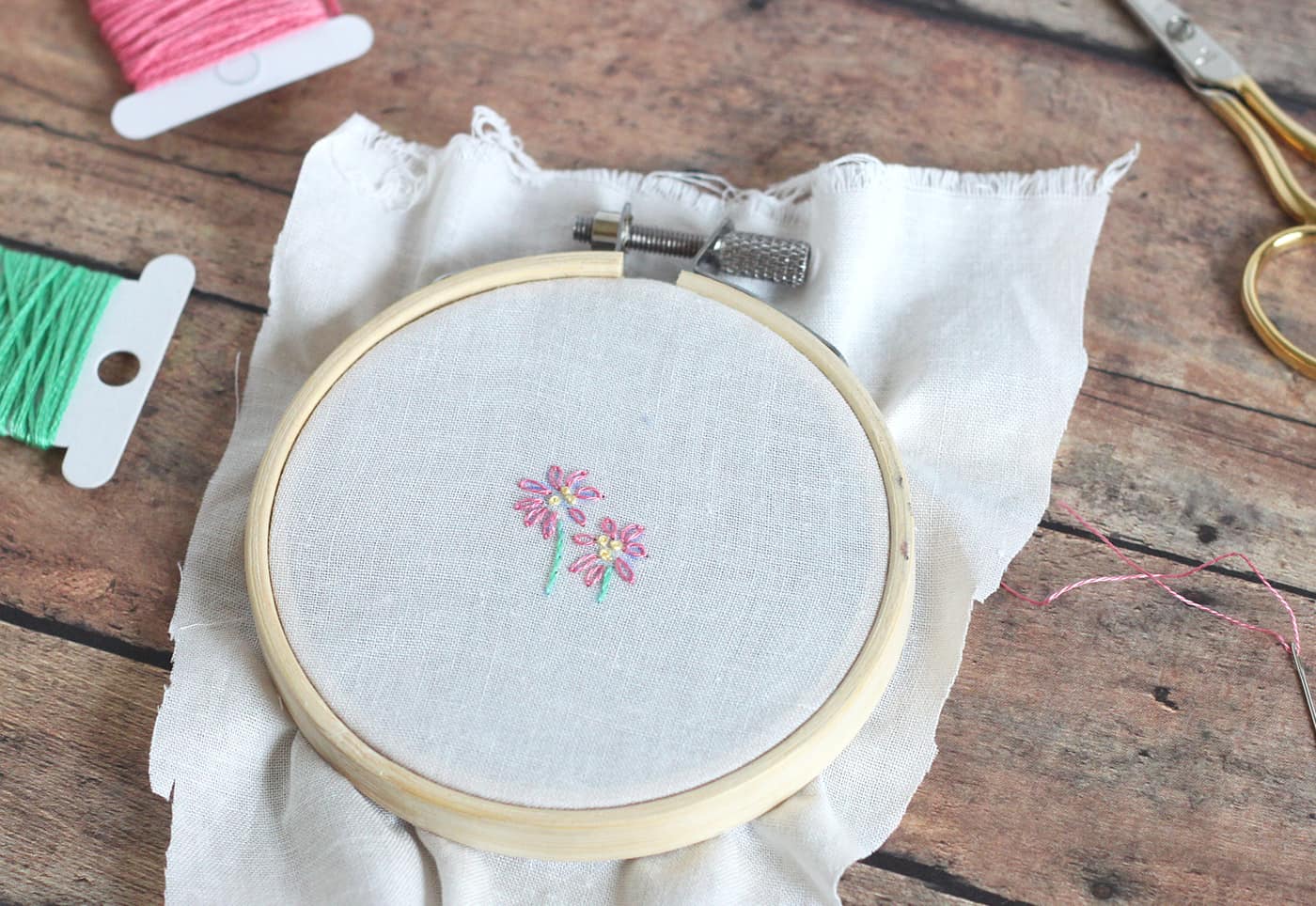 Pink flower with green stem stitched onto canvas in an embroidery hoop