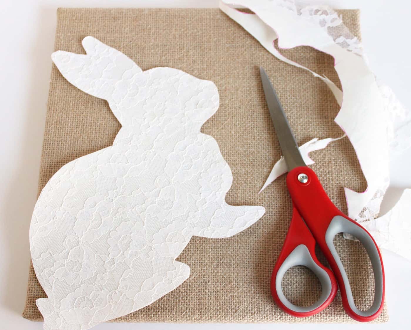 Lace rabbit shape cut out sitting on top of the burlap fabric with scissors