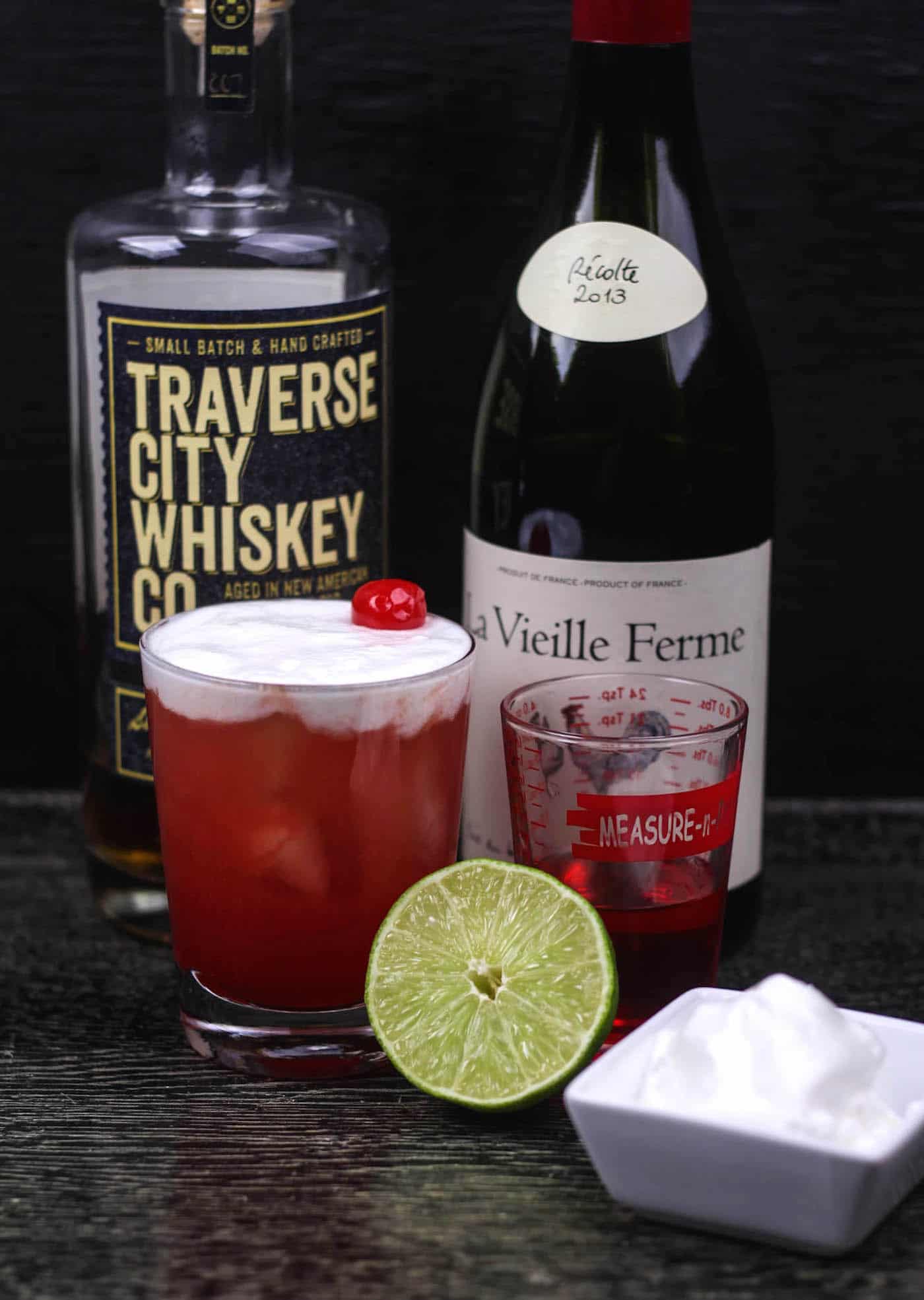 Bottle of Traverse City whiskey, cherry cocktail, and lime