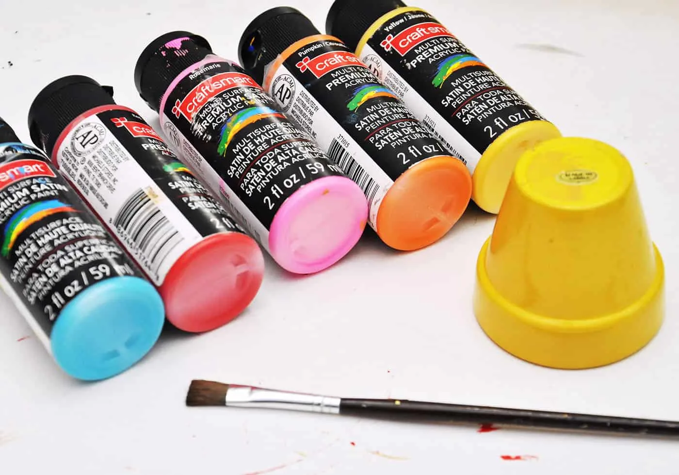 Various colors of craftsmart paint with a yellow painted flower pot