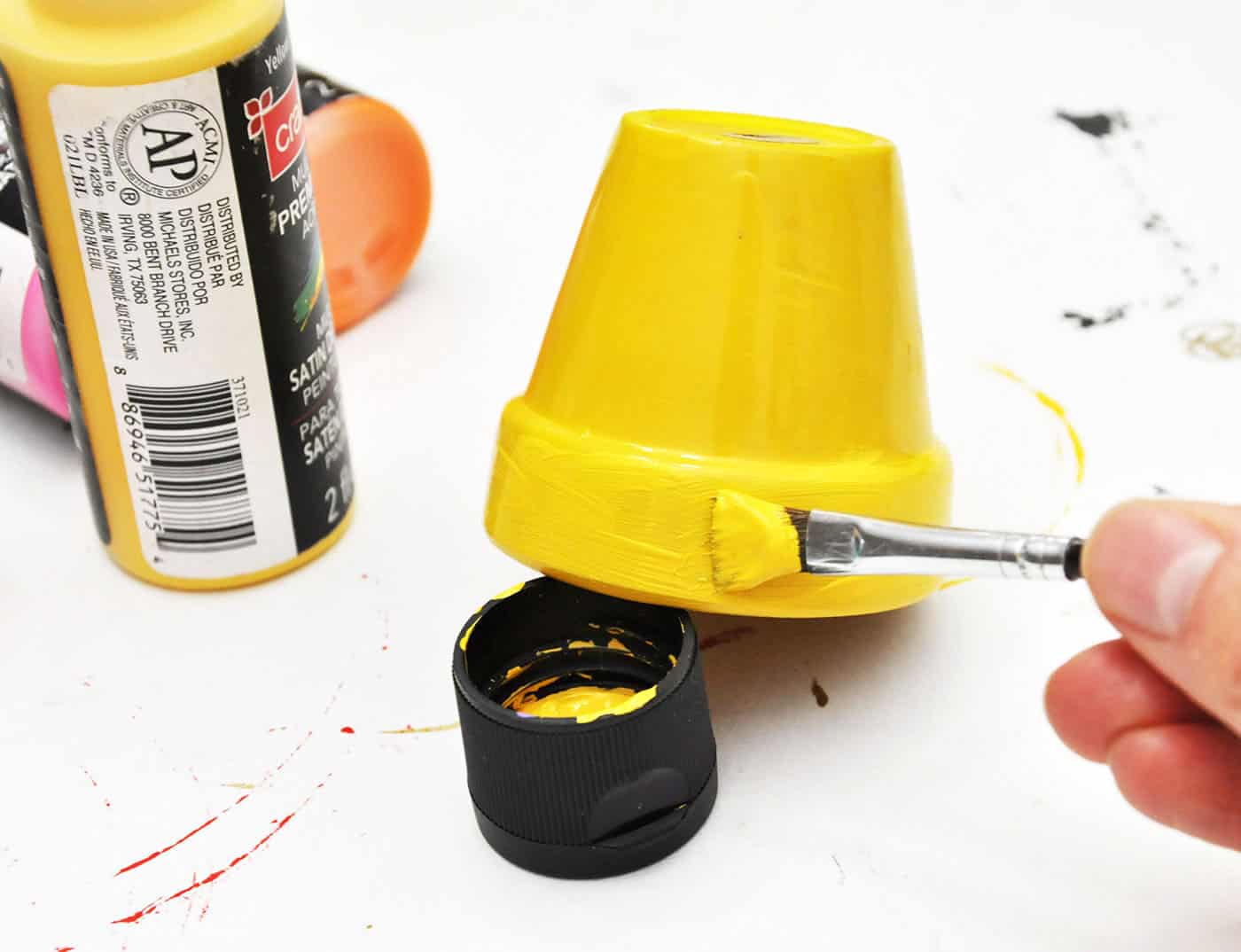 Painting a terra cotta pot with yellow paint using a paint brush