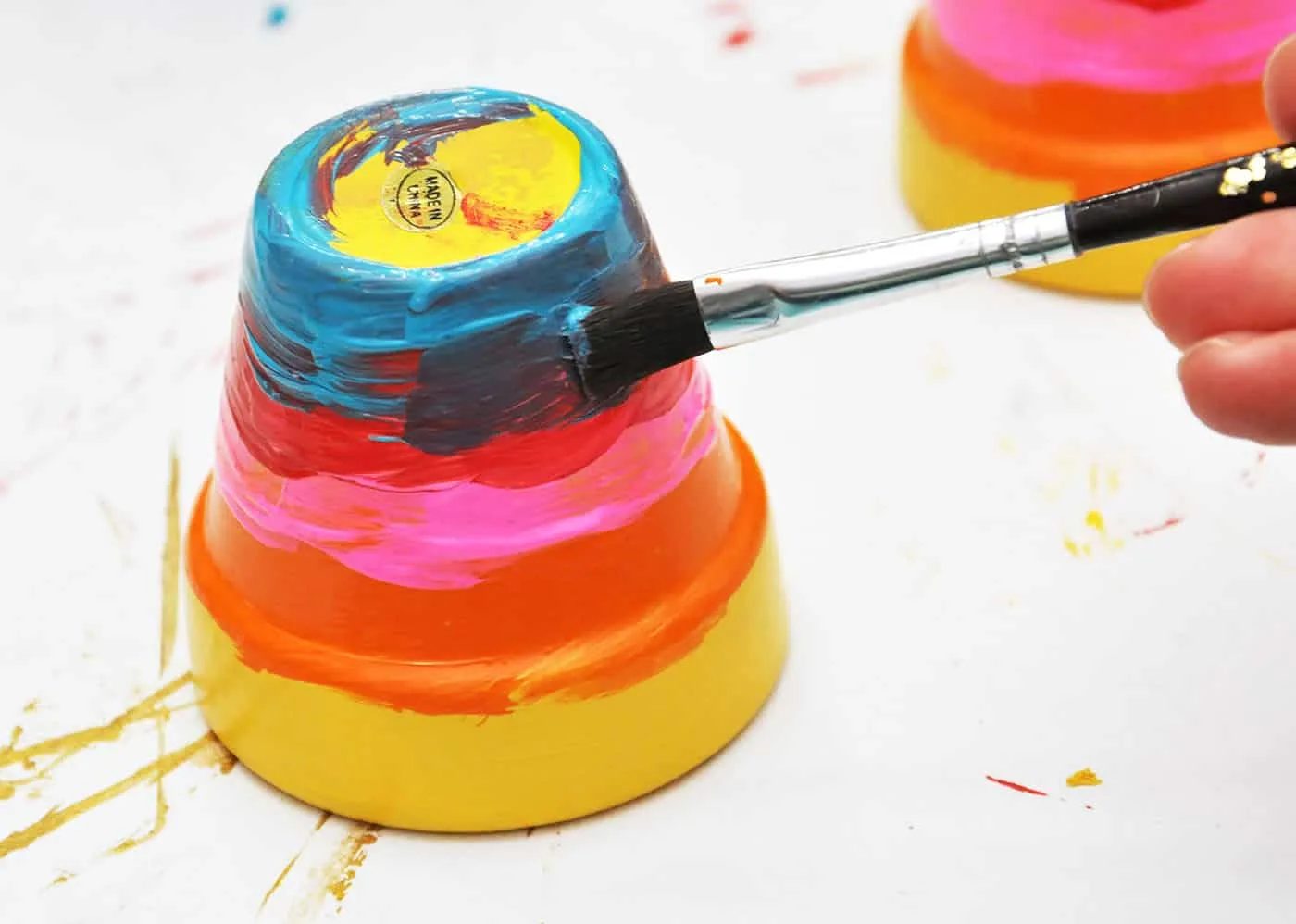 Painting a blue stripe on a rainbow pot