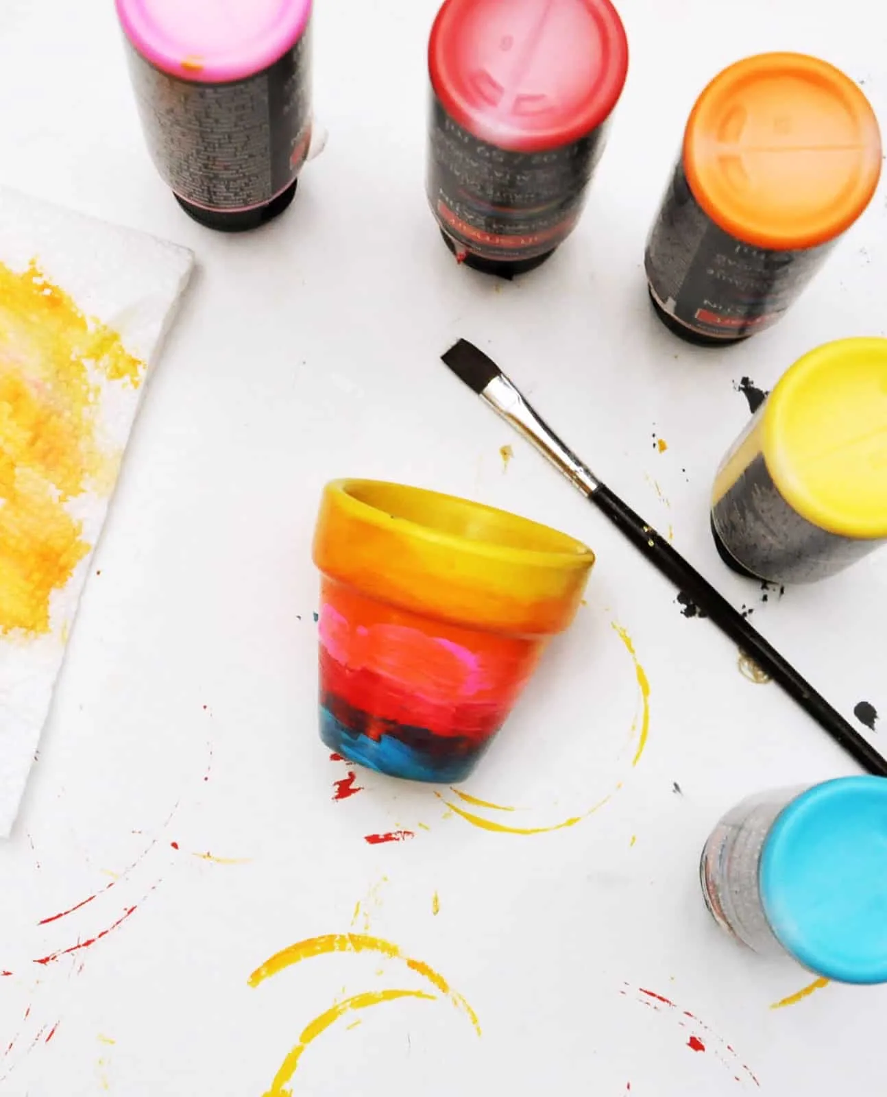 The bottom of four paint bottles and a painted pot with a paintbrush