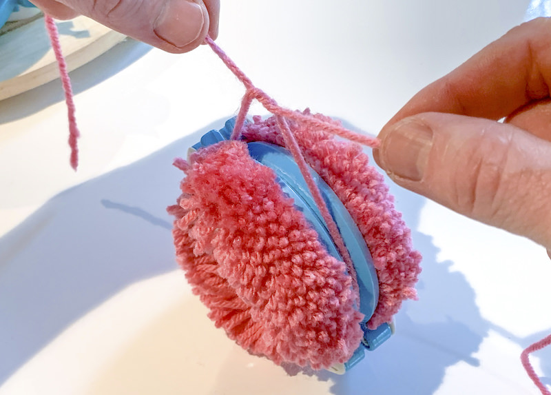 Tying a knot around a pom pom in a pom pom maker