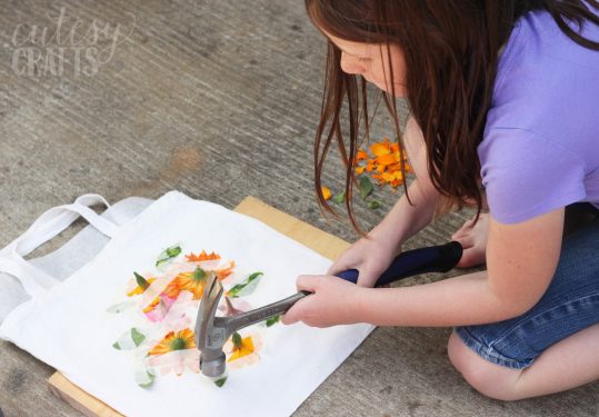 Child pounding flowers on a canvas tote with a hammer