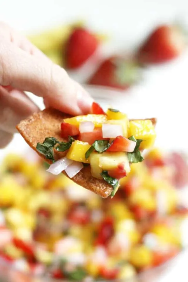 Easy mango salsa recipe with strawberries and basil on a tortilla chip