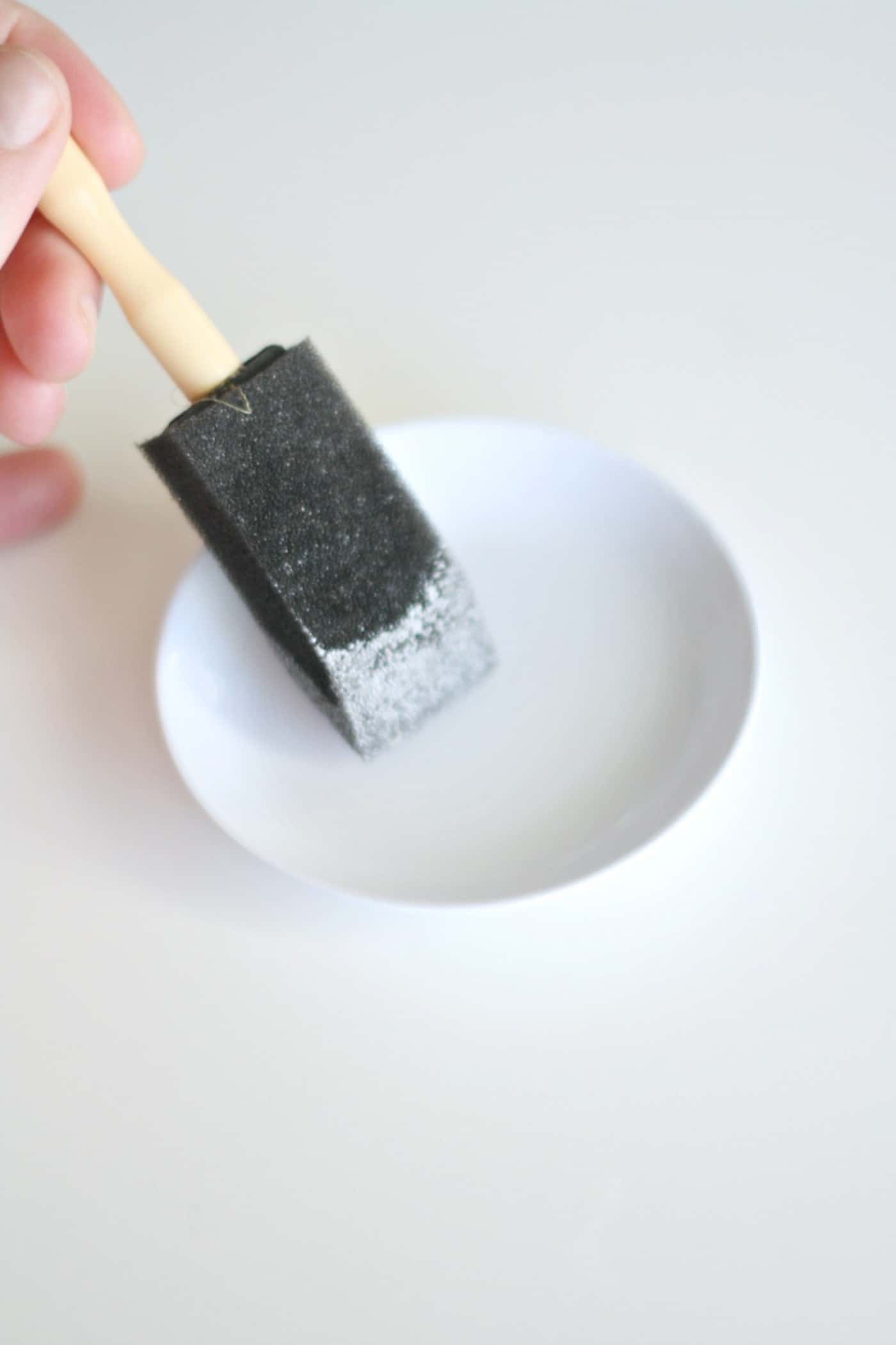 Applying a thin layer of Mod Podge to a ceramic dish with a foam brush