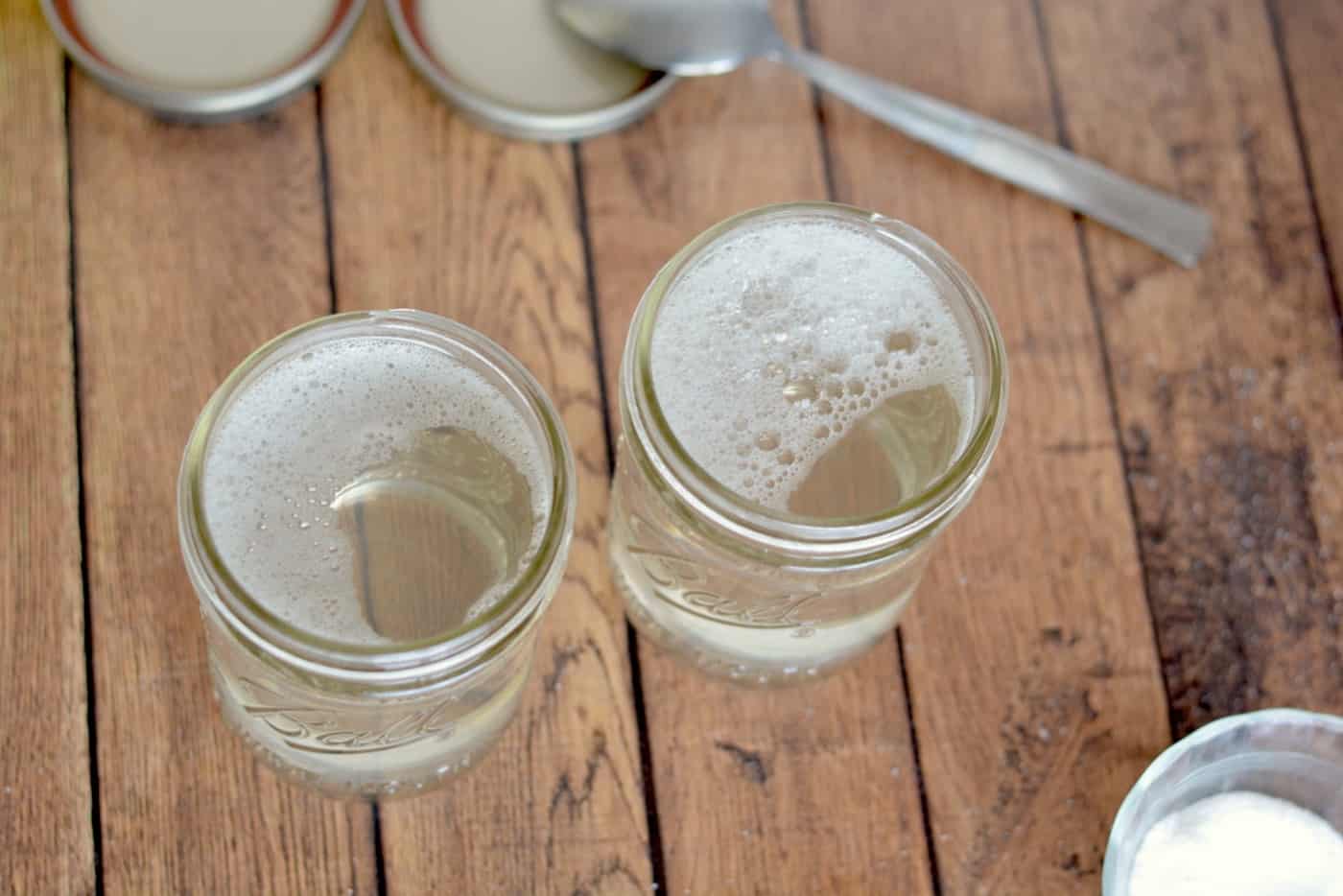 Two mason jars with liquid laundry detergent in them with the lids off on a wood background