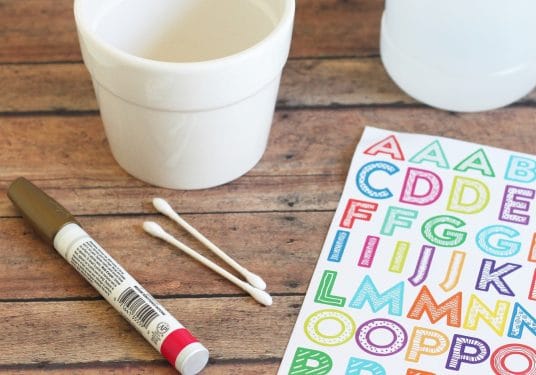 Oil based Sharpie marker, letter stickers, Q-tips, and a white ceramic pot on a wood surface