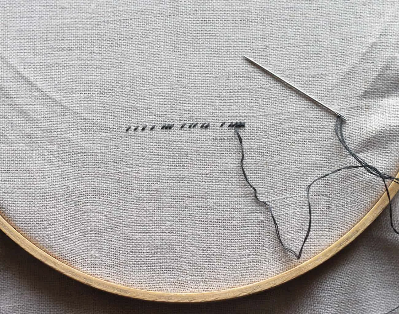 Linen in an embroidery hoop and stitching with black embroidery floss