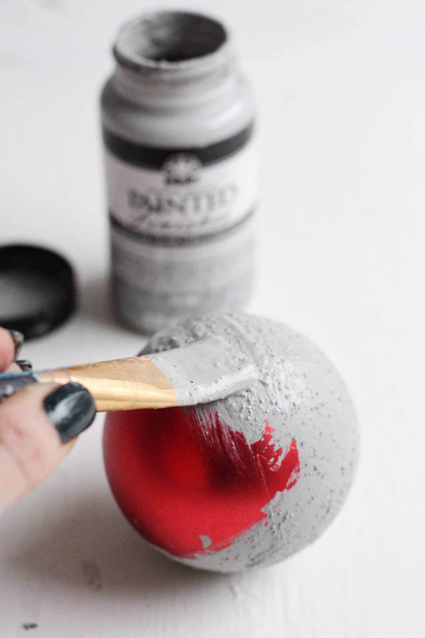 Painting a red Christmas ball ornament using concrete finish and a paintbrush