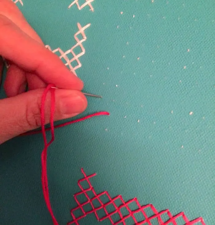 Cross stitching pink thread onto canvas