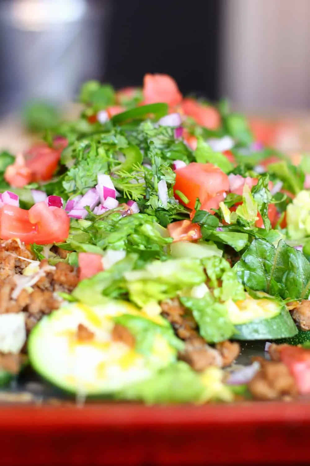Pile of zucchini nachos with fake meat crumbles, tomato, onion, and lettuce