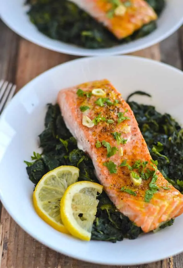 Baked salmon and spinach in a while bowl with lemon