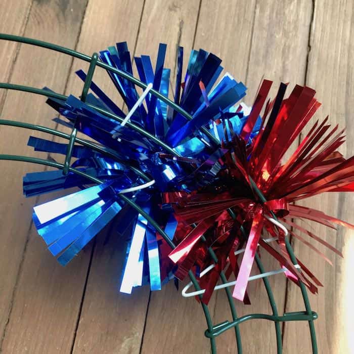 Wrapping red and blue metallic pom poms around a wreath form