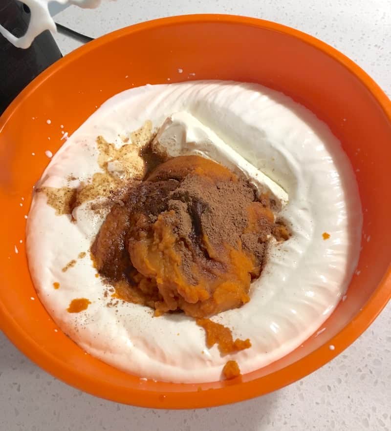 Cool whip, pure pumpkin, spices, vanilla extract, and cream cheese in an orange bowl